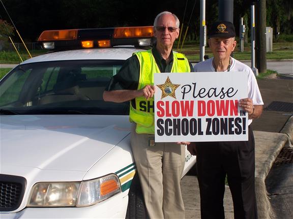 Volunteers holding drive safe in school zone sign